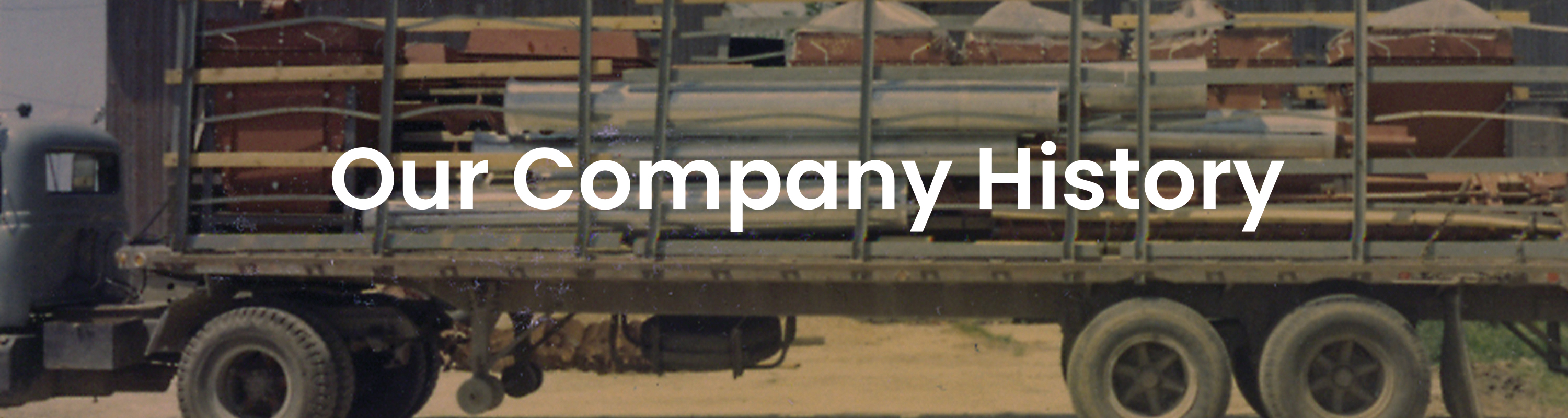 Old farm tractor trailer hauling reclaimer parts with white text overlay that reads OUR COMPANY HISTORY bulk material handling system, bridging, rat-holing, material flow, reclaim, reclaimer, silo unloading, unloader, bulk material storage, reclaim system, dry bulk unloading, grain unloading
