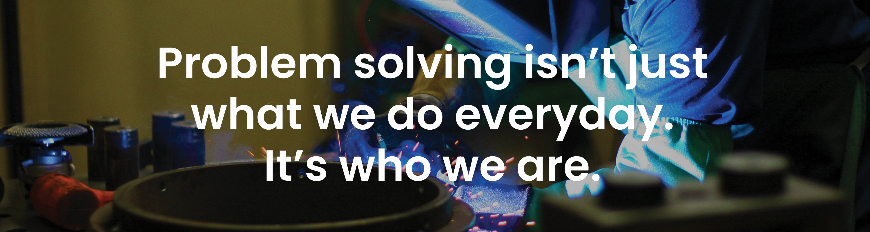 Dark background showing person welding with white text overlay that reads PROBLEM SOLVING ISN'T JUST WHAT WE DO EVERYDAY. IT'S WHO WE ARE. bulk material handling system, bridging, rat-holing, material flow, reclaim, reclaimer, silo unloading, unloader, bulk material storage, reclaim system, dry bulk unloading, grain unloading